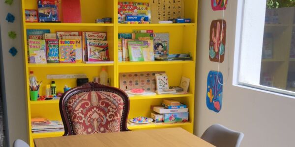 Picture of the dining and activities area at Oretha's Senior Daycare in SS3, Petaling Jaya. There is a dining table where the seniors can have their meals and mingle with each other. Behind the table is a shelf full of activity sheets, games for the seniors.